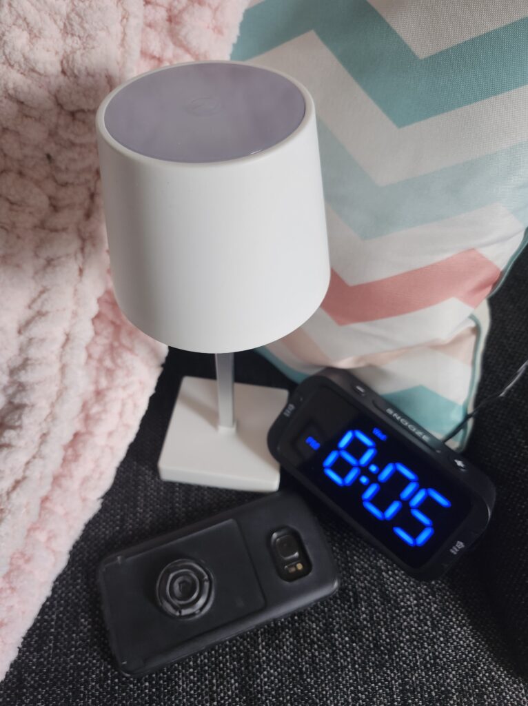 Phone turned down on a cozy bed with a lamp and some pillows and a blanket