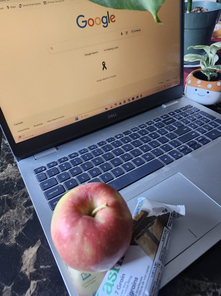Laotop open on table with a snack on the corner of the tanle