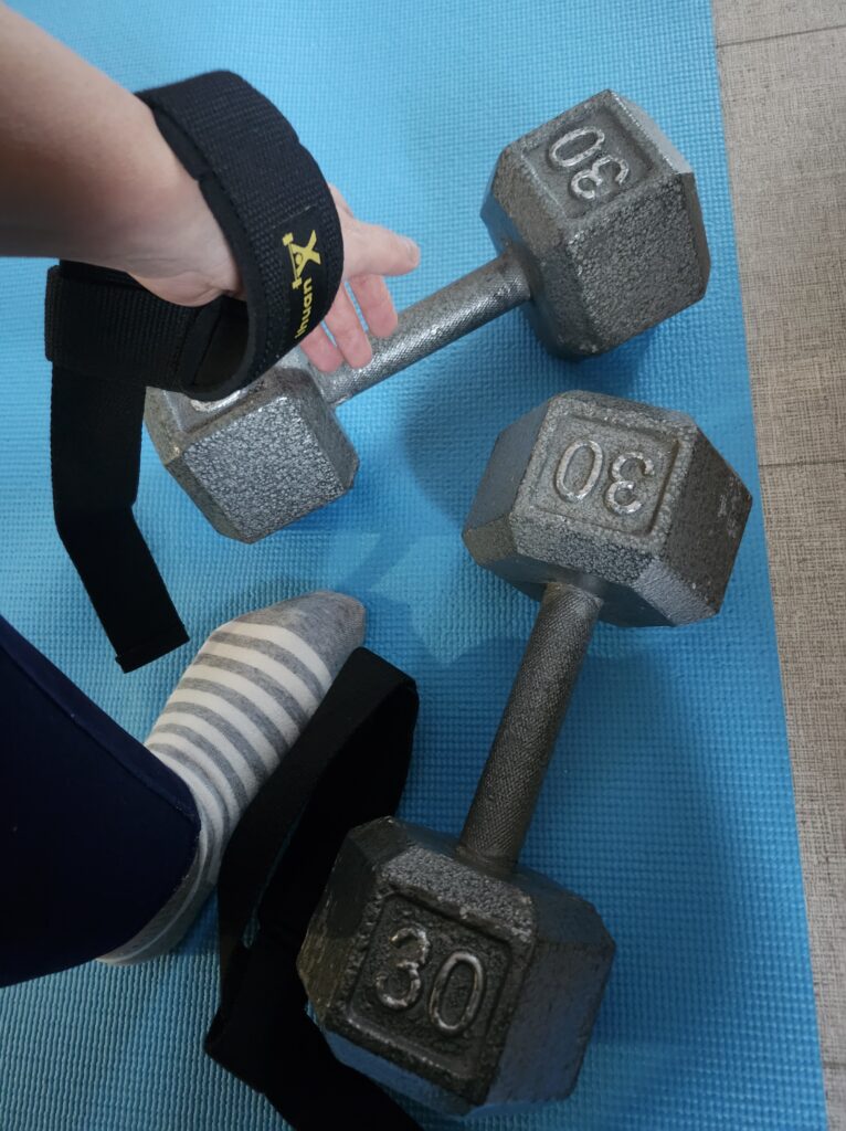 On a blue mat with dumbbells and arm with lifting straps